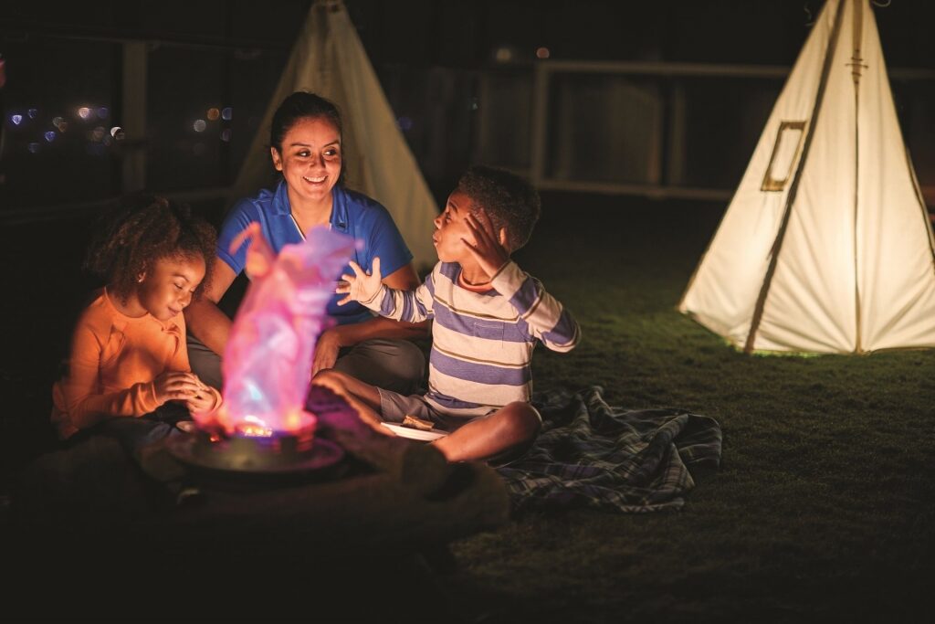 Woman and two kids camping out at Celebrity Cruises Lawn Club at night